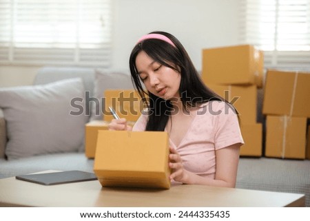 Startup small business owner working at home, woman writing address on parcel box at home for delivery order to customer, Online shopping business, ecommerce concept