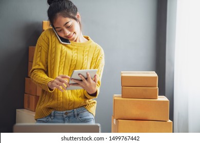 Startup small business SME, Entrepreneur owner using smartphone or tablet taking receive and checking online purchase shopping order to preparing pack product box. Selling online ideas concept