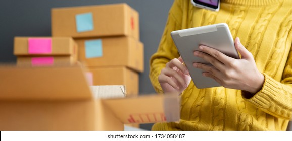 Startup small business SME, Entrepreneur owner using smartphone or tablet taking receive and checking online purchase shopping order to preparing pack product box. Selling online ideas concept