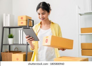 Startup small business, A young Asian woman checking online order on digital tablet and packing boxes for products to send to customers. working at the home office.