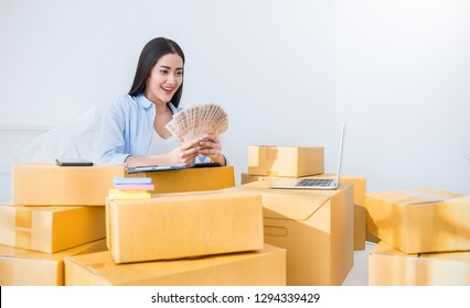 Startup SME Freelance Woman Holding Money Working At Home Office, Young Asian Small Business Owner Use Computer, Online Marketing Packing Box Delivery, SME E-commerce Bill Telemarket Success Concept  