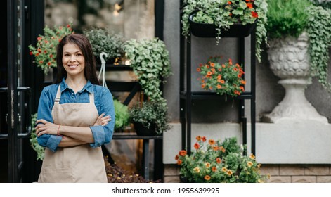 Startup successful small business, entrepreneur standing at florist shop, environment friendly concept. Caucasian lady owner, smiling confident millennial woman in apron with crossed arms near store