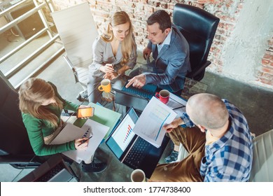 Startup Team Of Businesspeople Looking At Business Plan Financials, Top Down View