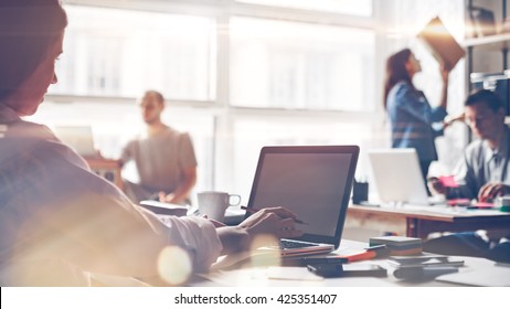 Startup team at work. Big open space office, laptops and paperwork. Business concept. Film effect and lens flare effect, blurry background - Shutterstock ID 425351407