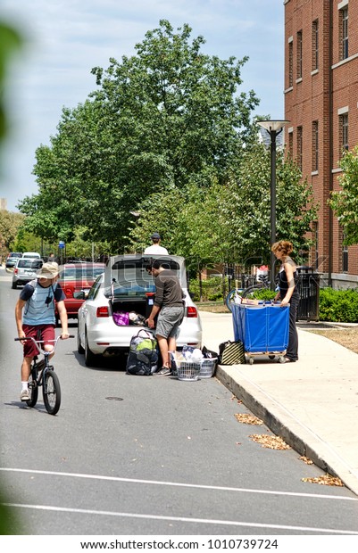 State\
College, Pennsylvania, August 10, 2016 - A woman helps a male\
student unload his car on move-in day at the main campus of Penn\
State University as a bicyclist glances\
back.