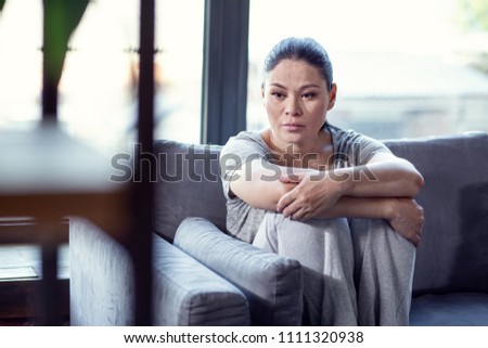 State of depression. Forlorn despaired woman sitting on sofa and hugging knees