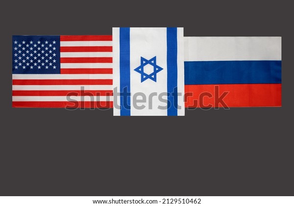 State flags of the\
USA, Russia and between them Israel on a dark background close-up.\
Copy space. Flags