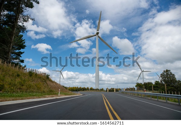 State highway heading  beneath the giant Wind\
turbines generating electricity on the hills of a rural\
agricultural farm