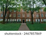 A stately brick building with large windows and a central entrance is surrounded by well-maintained lawns and trees.