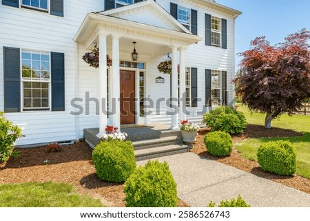 Stately colonial style estate home set agains beautiful blue sky expansive yard landscaping American flag barn shop gravel driveway pillars front entrance door welcoming white house green grass summer
