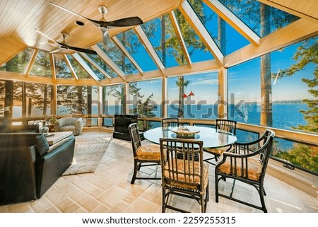 stately and elegant living room of a waterfront home interior space with wall of windows and sky lights with bright colourful skies at sunset and dusk blue hour rich leather chairs fireplace