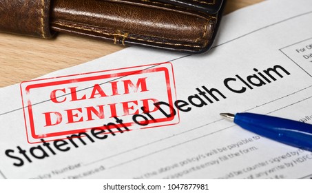 Statement Of Death Claim Form On A Wooden Surface. Next Is A Blue Fountain Pen, Leather Purse. On The Form Is A Red Stamp Claim Denied

