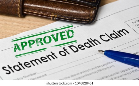 Statement Of Death Claim Form On A Wooden Surface. Next Is A Blue Fountain Pen, Leather Purse. On The Form Is A Green Stamp Approved

