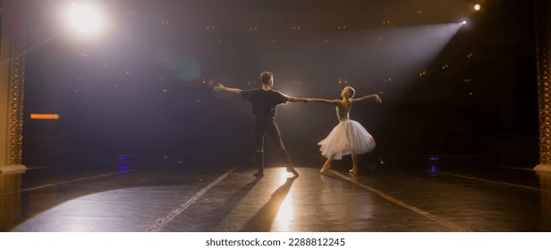 Static full shot of ballet dancers practicing graceful ballet movements and rehearse choreography on classic theater stage illuminated by spotlights. Dance partners prepare theatrical performance. - Powered by Shutterstock - Get 15% off with code: PIKWIZARD15