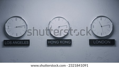 Static shot of white wall clocks with running time pointers illuminated by lamp in office with modern design. Names of big cities written under wall clocks. Watches showing time of different cities.