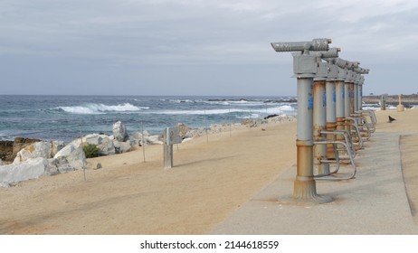 Stationary binoculars, telescope, tower viewer or scope, ocean waves on rocky craggy beach. Magnifier or spyglass row, 17-mile drive tourist viewpoint, Monterey, California USA. Bird Rock Vista Point.