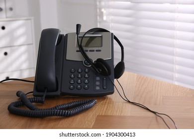 Stationary phone and headset on wooden table indoors. Hotline service