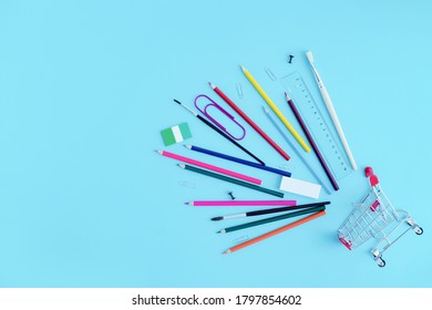 Stationery, Colored Pencils Sprinkled From A Shopping Cart On A Blue Background, Top View. Copy Space. Back To School Shopping With Stationery