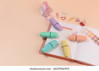 Stationery items in pastel colors arranged on open notebook with clips and washi tape at a workspace