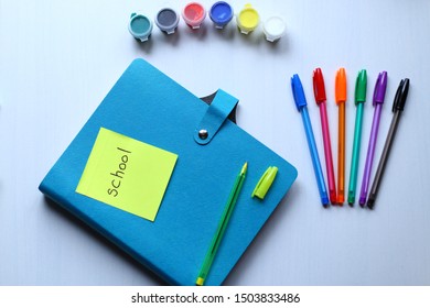 Сomposition of stationery: multi-colored pens and paints, blue copybook and yellow pen with a cap