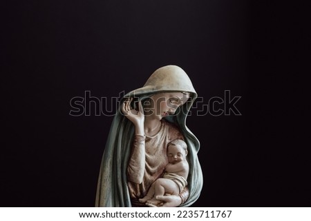 Statue of baby Jesus held in the arms of the Virgin Mary in the middle of the frame against a black background with copy space