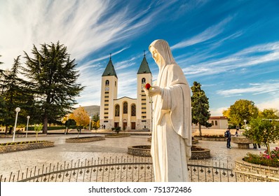 statue of the Blessed Virgin Mary holding a red rose while Saint James Church in Medjugorje is in background