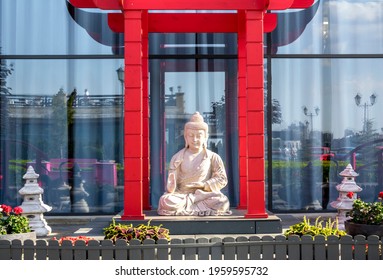Statue of Buddha (also known as Siddhartha Gautama, Shakyamuni Buddha) sitting in meditation in the garden under red asian arch paifang, pailou