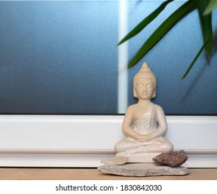 Statue Of Buddha On Window Sill With Granite And Quartz Stones And Green Leaves