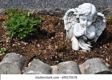 Statue Of A Child Angel In A Cemetery Above A Grave