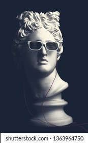 Statue. Earphone. Isolated. Gypsum statue of Apollo's head. Man. Creative. Plaster statue of Apollo's head in earphones and white sunglasses. Head.