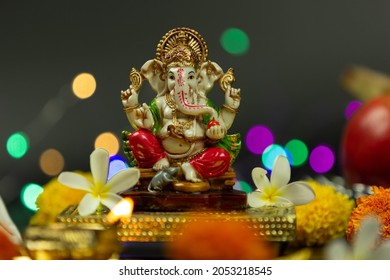 Statue Of Ganpati Bappa Morya Hindu God Ganesha Sitting On Golden Asana With Fruits, Flowers, Lamp, Shunkh And Blur Bokeh For Diwali Puja New Year Deepawali Ganesh Chaturthi Or Shubh Deepavali Pooja