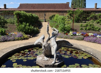 Statue Of A Girl And A Swan In A Lily Pond In The Walled Garden Of An Old English Country Manor House