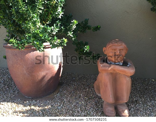 Statue\
of a Grumpy Old Man Sitting Next to a Potted\
Plant
