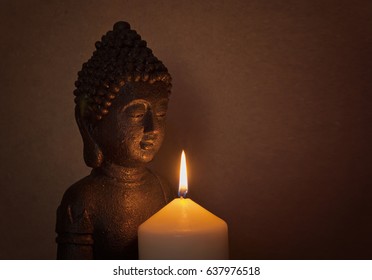 Statue of a holy Buddha in the light of a candle on a wooden background