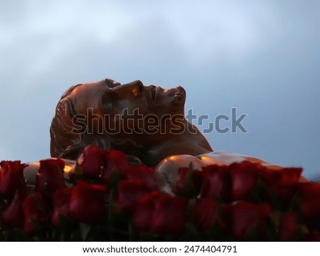 Statue of jesus christ lying down surrounded by red roses, in a spiritual atmosphere
