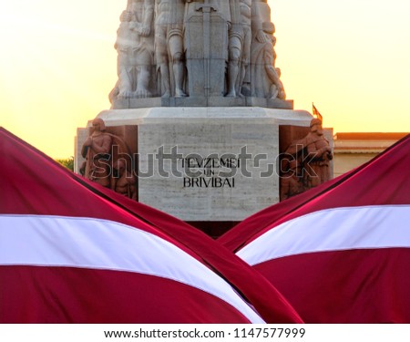 Statue of Liberty in Riga, background filled with the state Latvia flag , sunrise behind of monument