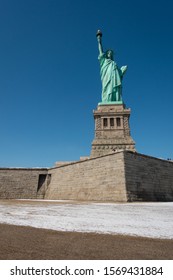 Statue Of Liberty, Shot At Liberty Island In Wintertime With Snow And Pedestal Visible. Shot In Sunny Daylight With Clear Blue Sky.