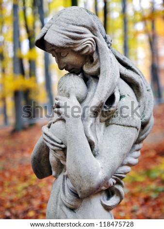 Statue of Madonna and child in autumn forest at cemetery