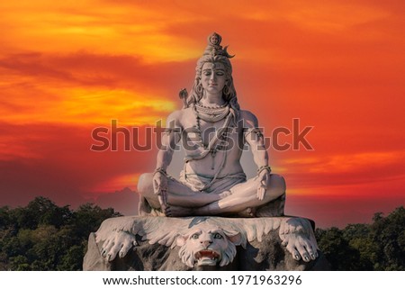 Statue of meditating Hindu god Shiva against the red sky on the Ganges River at Rishikesh village in India, close up