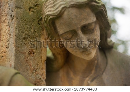 Statue of a sad woman on a cementery mourning over the grave. Closeup of face of statue looking like a female angel. Hand of woman is hugging a stone column next to her.
