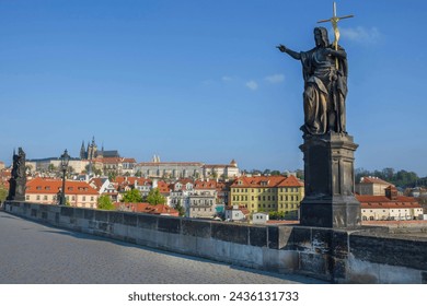 Statue of St. John the Baptist on Charles Bridge, with Hradcany castle and St. Vitus Cathedral in the background, in Prague, Czech Republic, in sunny day