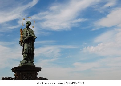Estatua de San Juan de Nepomuk, puente Carlos, Praga. Cielo azul con nubes blancas.
