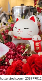A statue of a white lucky cat. accompanied by a blushing red flower