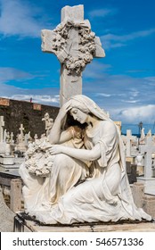 Statue Of Woman Kneeling At Grave With Cross Behind Her With Wreath Of Flowers