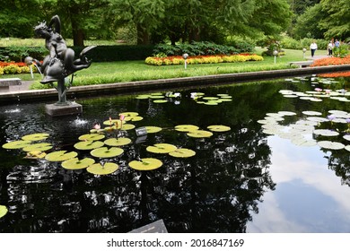 A Statue Of A Woman Riding A Bird. The Statue Is In A Pond At The Missouri Botanical Garden In St. Louis. People Are Walking On The Paths. Picture Taken On July 19th, 2021.