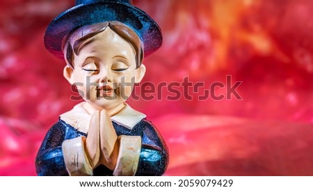Statue of a young pilgrim boy giving thanks on an orange background.