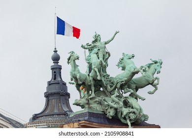 Statues on the Grand Palais in Paris .  Bronze statue of flying horses and chariot . French flag on the top 