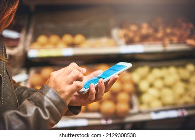 Status Update Doing The Weekly Grocery Run. Cropped Shot Of A Woman Using A Mobile Phone In A Grocery Store.