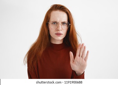 Stay Away From Me. Angry Irritated Young European Red Haired Woman In Turtleneck And Eyewear Reaching Out Her Palm, Showing Stop Gesture, Doesn't Want To Continue Conversation, Fight Or Quarrel