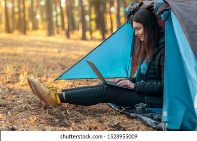 Stay connected. Young girl using laptop in camping tent, hiking in autumn forest, empty space - Powered by Shutterstock